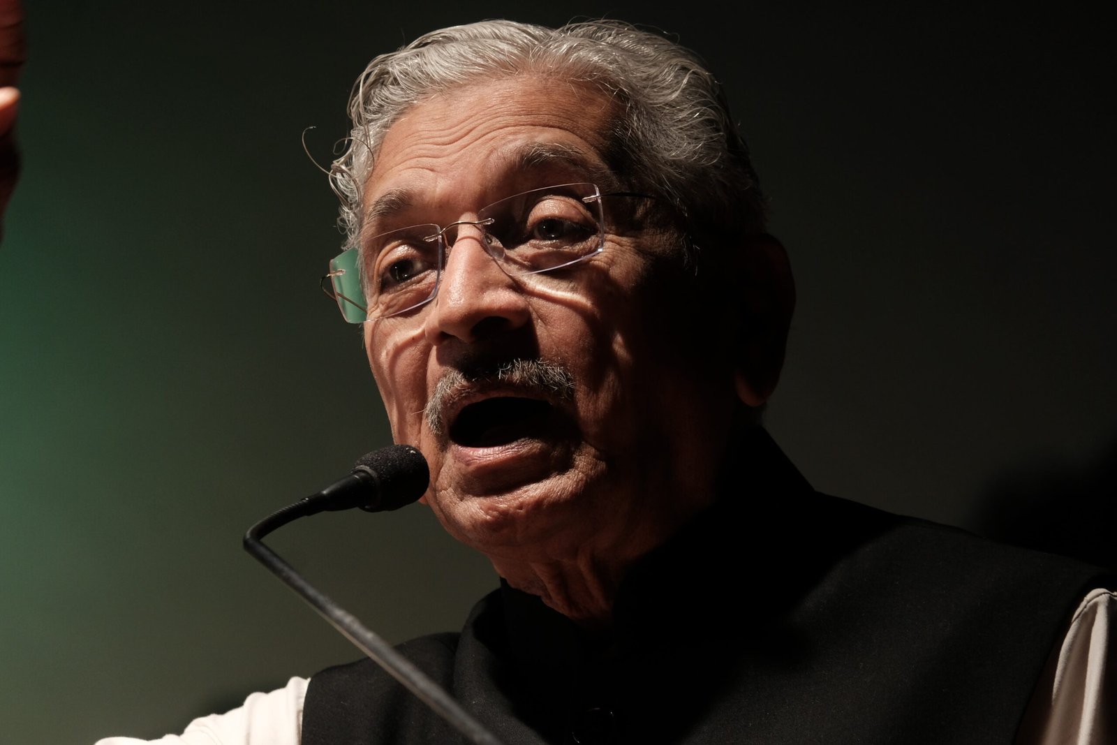 a man with glasses and a mustache speaking into a microphone